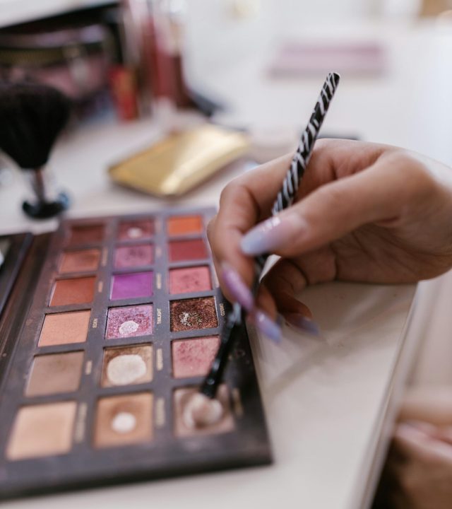Close-up of a hand using a makeup brush on a colorful eyeshadow palette.